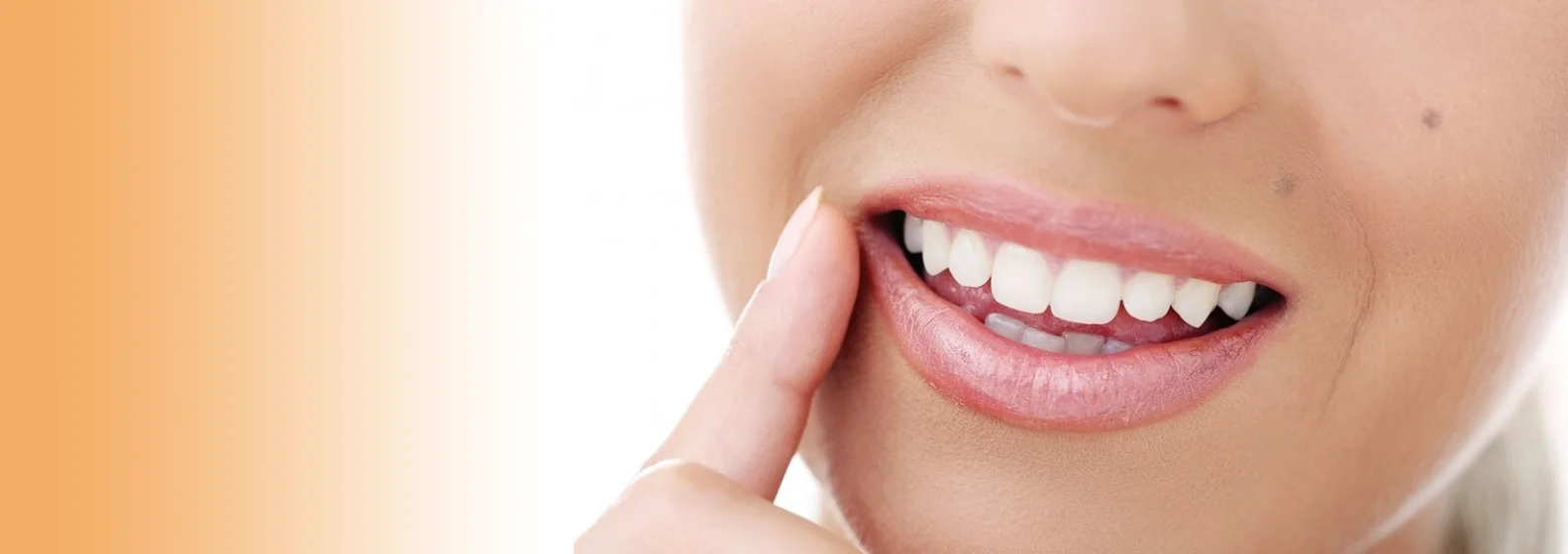 Close-up of a smiling person pointing to their bright white teeth, set against an orange gradient background.
