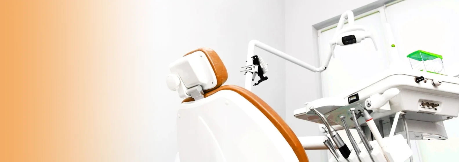 Modern dental chair and equipment in a bright clinic with an orange gradient on the left.